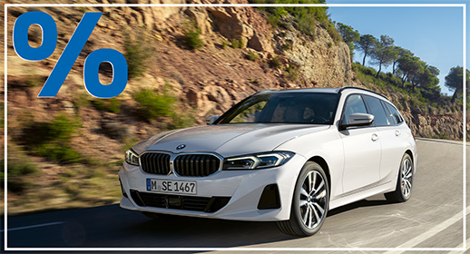 Das Bild zeigt einen weißen BMW 3er-Reihe Touring (Kombi), der auf einer kurvigen Straße fährt. Das Auto ist schräg von vorne zu sehen. Im Vordergrund ist ein großes, rotes Prozentzeichen (%) platziert. Der Hintergrund zeigt eine bergige Landschaft mit Bäumen und Sträuchern. Das Kennzeichen "M SE 1467" ist auf der vorderen Stoßstange zu sehen.