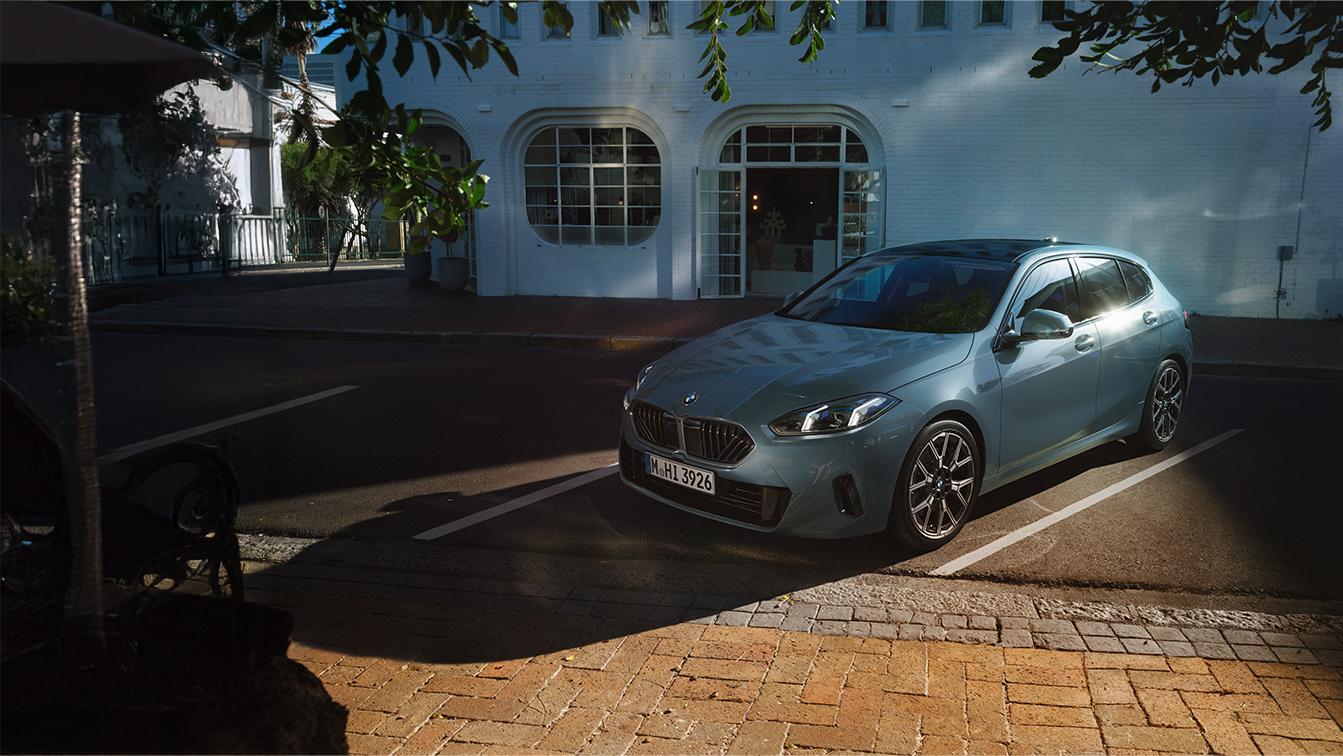 Hellblauer BMW 1er in Front-Seitenansicht, geparkt an einer Straße vor einem weißen Gebäude.