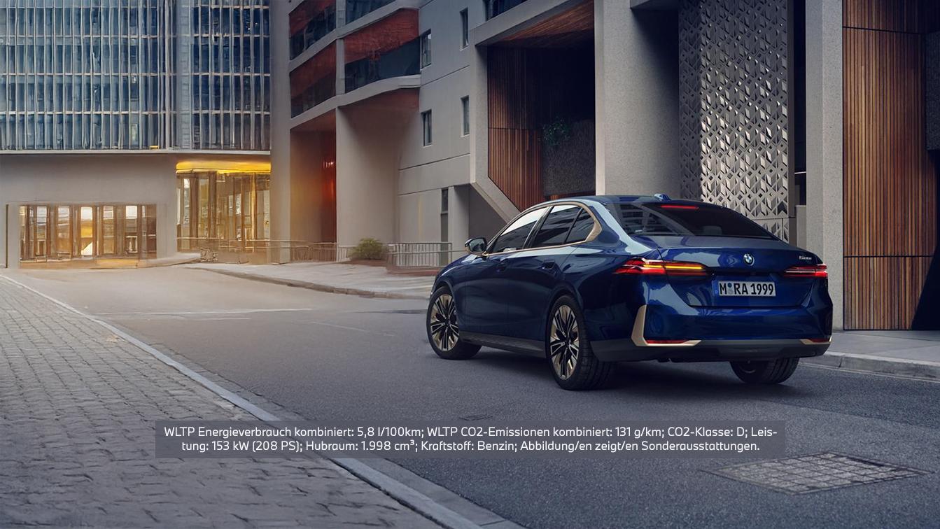 Eine dunkelblaue BMW 520i Limousine ist von hinten rechts auf einer Straße vor modernen Gebäuden geparkt. Das Fahrzeug hat ein Kennzeichen mit der Aufschrift "M RA 1999" und zeigt die Rückleuchten sowie leichte Chromakzente. Im unteren Bereich des Bildes befindet sich eine Texteinblendung mit folgenden technischen Daten: "WLTP Energieverbrauch kombiniert: 5,8 l/100km; WLTP CO2-Emissionen kombiniert: 131 g/km; CO2-Klasse: D; Leistung: 153 KW (208 PS); Hubraum: 1.998 cm³; Kraftstoff: Benzin; Abbildung/en zeigt/en Sonderausstattungen.