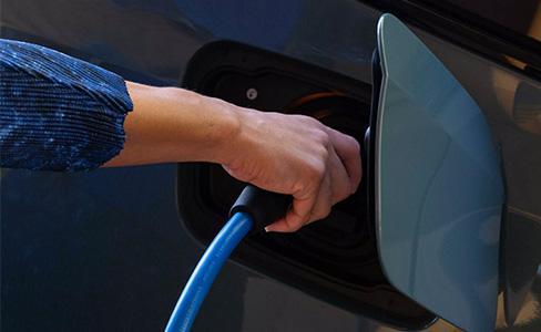 Hand steckt blaues Ladekabel in BMW Elektroauto.