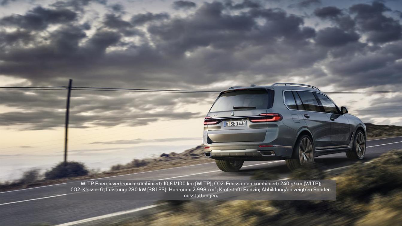 Ein seitlich-hinten aufgenommenes Bild eines grauen BMW X7, der auf einer leeren Straße bei Dämmerung oder Bewölkung fährt. Das Fahrzeug bewegt sich weg vom Betrachter, seine Rückleuchten und die Heckpartie sind gut sichtbar. Im Hintergrund ist eine weite, offene Landschaft mit einem bewölkten Himmel und einer Andeutung von Sonnenuntergang oder Aufgang zu sehen. Links im Bild steht ein Strommast oder eine Telefonleitung. Das Kennzeichen des Fahrzeugs lautet "M SE 1438".  Über dem Bild ist ein Textoverlay mit folgenden Informationen: WLTP Energieverbrauch kombiniert: 10,6 l/100 km (WLTP); CO2-Emissionen kombiniert: 240 g/km (WLTP); CO2-Klasse: G; Leistung: 280 kW (381 PS); Hubraum: 2.998 cm³; Kraftstoff: Benzin; Abbildung/en zeigt/en Sonderausstattungen.
