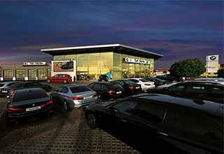 Autohaus Rhein Tief-Dörfler mit BMW-Logo bei Dämmerung und parkenden Autos.