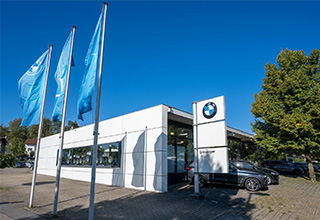  Modernes weißes BMW Autohaus mit blauen Flaggen und parkenden Autos